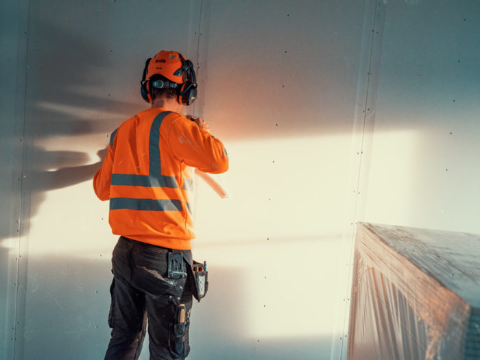 Hantverkare med skyddshjälm och hörselkåpor monterar väggskivor.
