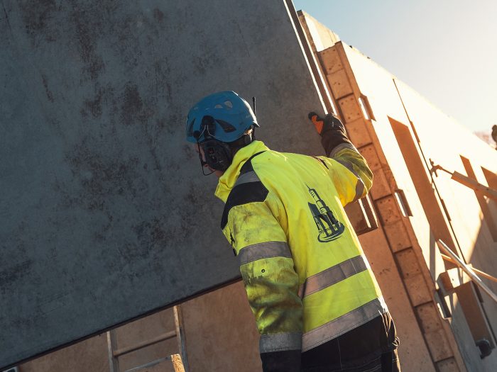 Bild på byggarbetare som håller i ett betongblock. Han har handskar på sig. 
